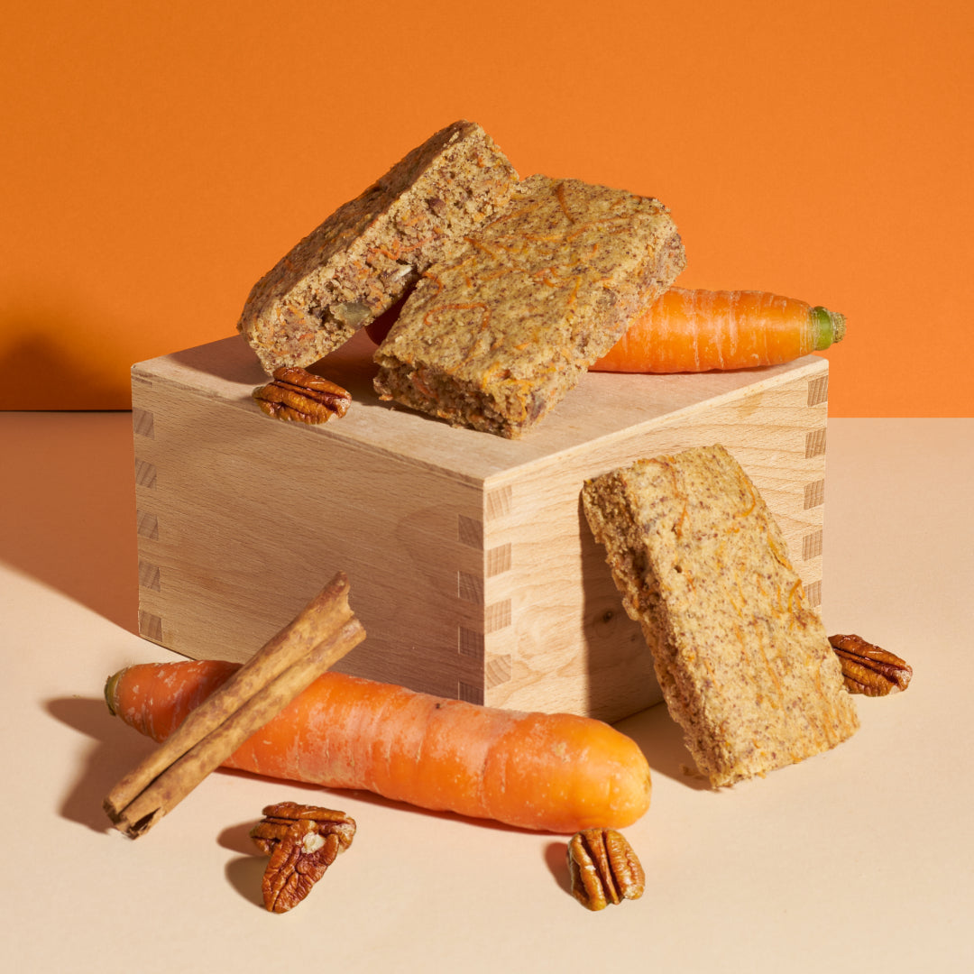 Karotte-Pekannuss Kuchen drapiert mit Karotten, Zimtstange und Pekannüssen auf Holzbrett