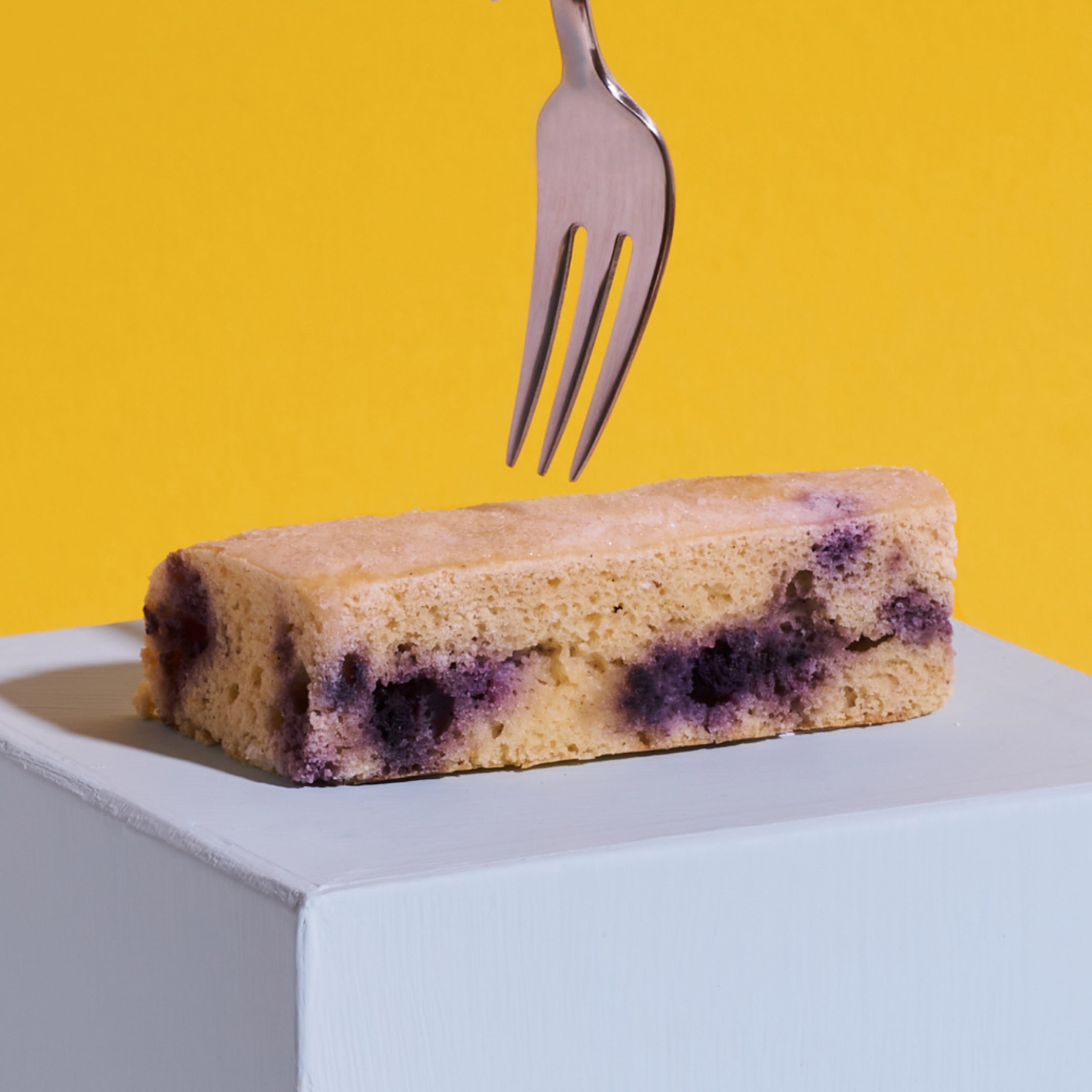 Ein Stück Zitrone-Blaubeer Kuchen als Nahaufnahme mit einstechender Gabel